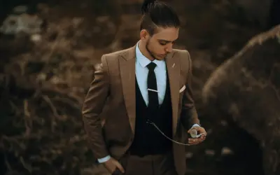 Stilberatung für Senioren: Mode ab 60. Ein Mann im eleganten braunen Anzug mit Weste und Krawatte hält eine Taschenuhr.