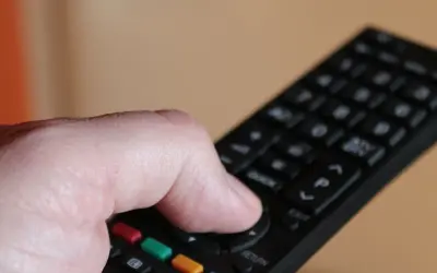 Dłoń naciska przycisk na pilocie, by dowiedzieć się, jak odbierać wszystkie kanały telewizji naziemnej.