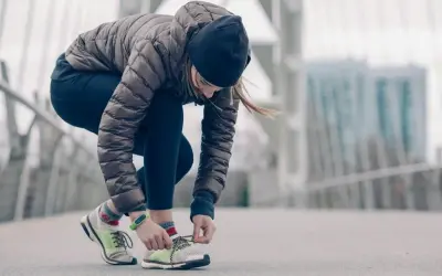 Une femme en tenue de running hiver attache ses lacets sur un pont.