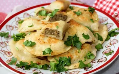 Talerz pełen złocistych pierogów z soczewicą, udekorowany świeżą natką pietruszki. Idealne na obiad!
