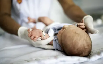 Delikatne badania neurologiczne noworodka. Ręce w rękawiczkach badają maleńkie dłonie i stopy dziecka.