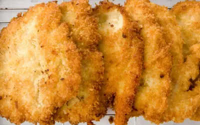 Fileteadas pechugas de pollo empanadas, doradas y crujientes, reposan sobre una rejilla metálica.