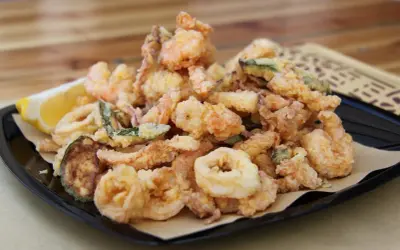 Un piatto invitante di frittura di pesce croccante, con gamberi, anelli di calamaro e verdure, accompagnato da uno spicchio di limone.