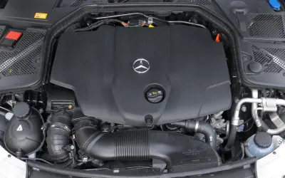 Silnik w Mercedesie C W205. Widoczna czarna osłona z logo producenta, przewody i elementy układu dolotowego.