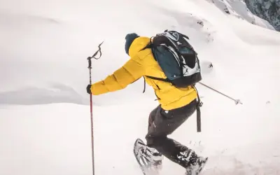 Person en raquettes, veste jaune vif, explorant un paysage enneigé. Les bâtons de randonnée aident à progresser dans la poudreuse.