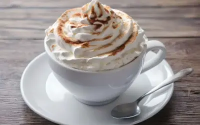 Ein cremiger Kapuziner Kaffee, üppig garniert mit Schlagsahne und Zimt, wartet auf einem Holztisch.