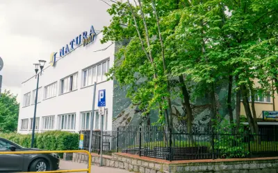 Dom wczasowy Radość, budynek z niebieskim napisem "NATURA tour", otoczony zielenią i ozdobiony mozaiką.