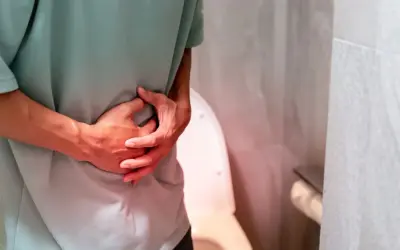 Osoba trzyma się za brzuch, odczuwając ból przy oddawaniu moczu. W tle widoczna jest toaleta.