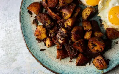 Knusprige bratkartoffeln aus rohen Kartoffeln, goldbraun gebraten, mit zwei Spiegeleiern auf einem rustikalen Teller.