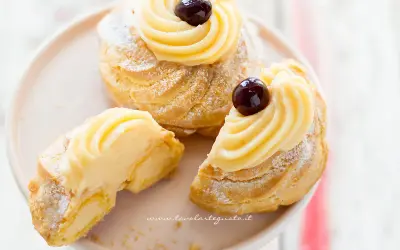 Zeppole di San Giuseppe, dolci soffici con crema pasticcera e ciliegina, uno è tagliato per mostrarne l'interno goloso.
