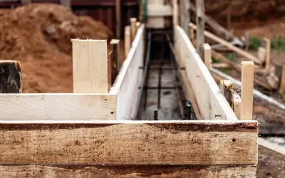 Drewniana szalunkowa konstrukcja przygotowana pod fundament pod ogrodzenie. W środku widoczna zbrojenie.