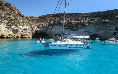 Catamarano "Respiro" in acque cristalline di un'isola sotto la Sicilia, con scogliere rocciose e altre barche.