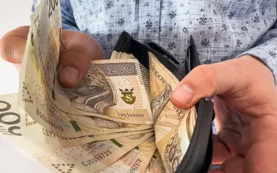 Ręce trzymają portfel z banknotami 200 zł. Ile trzeba przepracować, by tyle zarobić?