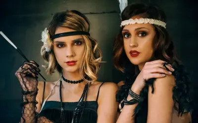 Dwie kobiety w stylu wielki gatsby stylizacja. Jedna z nich trzyma cygarniczkę, druga ma pióro we włosach.