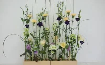 Kompozycja w stylu wegetatywnym we florystyce: delikatne kwiaty, trawy i liście tworzą naturalny, lekki ogród w prostokątnej donicy.