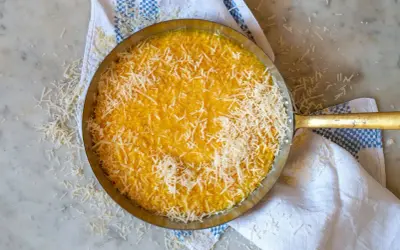 En gyllene risotto milanese, toppad med riven parmesan, i en metallpanna på en marmorskiva.