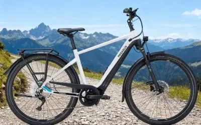 Ein weißes Pegasus E-Bike mit Gepäckträger steht auf einem Schotterweg vor einer Bergkulisse. Perfekt, um das E-Bike zu testen.