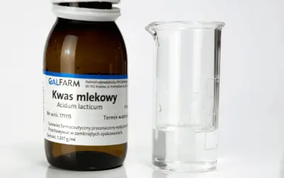 Butelka z napisem "Kwas mlekowy" i zlewka z płynem. Czy kwas mlekowy jest szkodliwy? Zależy od stężenia i zastosowania.