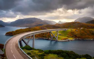 Un puente moderno cruza un fiordo escocés, con colinas otoñales y cielos dramáticos. La ruta 500 escocia ofrece vistas espectaculares.
