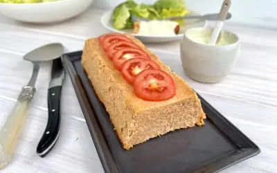 Un pain de thon savoureux, garni de rondelles de tomate fraîche, prêt à être dégusté avec une salade verte et une sauce crémeuse.