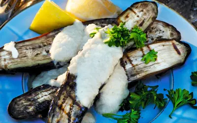 Grillad aubergine med en krämig sås och färsk persilja, serverad med citronklyftor. En härlig sommarrätt.