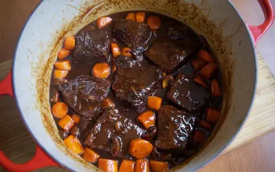 Boeuf bourguignon cocinado a fuego lento en una olla roja, con trozos de carne tierna, zanahorias y champiñones en una rica salsa.