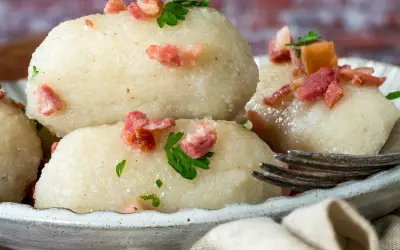 Pyszne pyzy z mięsem, posypane skwarkami i natką pietruszki, czekają na widelcu.