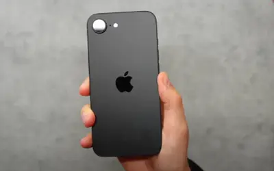 Czarna obudowa iPhone SE 4 z charakterystycznym jabłkiem Apple. Telefon trzymany w dłoni na szarym tle.
