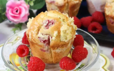Pyszne muffinki z malinami, posypane kruszonką, otoczone świeżymi malinami.