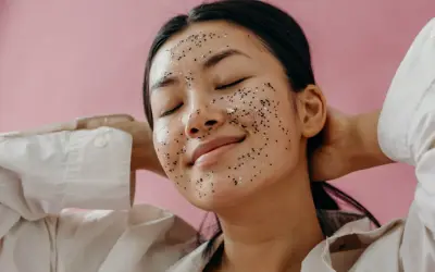 Une jeune femme au visage couvert d'un masque exfoliant scintillant, profitant d'un moment de détente. Elle nous rappelle pourquoi exfolier sa peau est essentiel pour un teint éclatant.