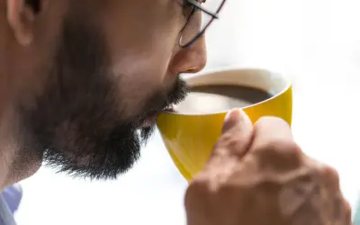 Man med glasögon dricker kaffe ur en gul mugg. Koffein ger energi, motverkar adenosin.