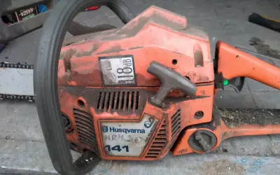 Pomarańczowa piła łańcuchowa Husqvarna 141, z widocznymi danymi technicznymi, gotowa do pracy.