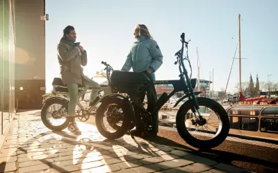Twee mensen bij hun fatbikes aan het water. De vraag "hoe zwaar is een fatbike" komt op, maar deze stoere e-bikes lijken verrassend licht.