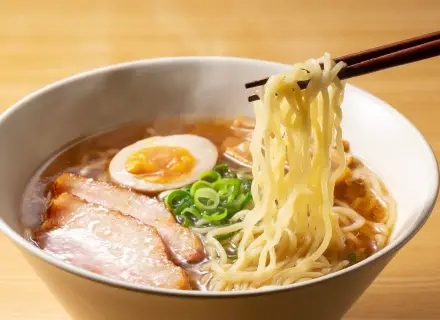 Parujące miseczka ramenu z makaronem, plastrami mięsa, jajkiem i szczypiorkiem. Idealne ramen przyprawy podkreślają smak.