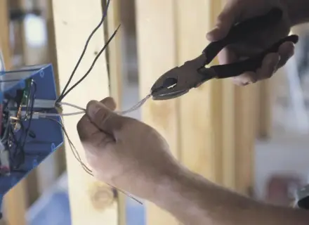 Ręce przycinają przewody do skrzynki elektrycznej. To kluczowy krok, by dowiedzieć się, jak zostać elektrykiem.