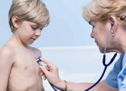 Lekarz osłuchuje klatkę piersiową chłopca, diagnozując zapalenie oskrzeli u dzieci.