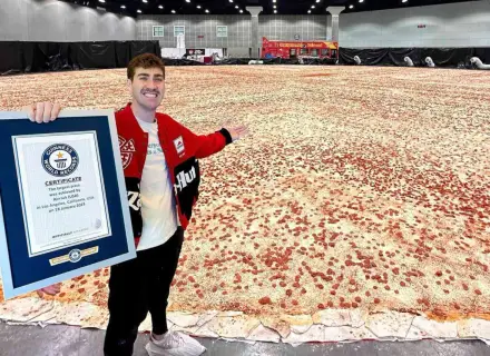 Mężczyzna prezentuje certyfikat Guinnessa za największą pizzę świata, która rozciąga się na ogromnej przestrzeni.