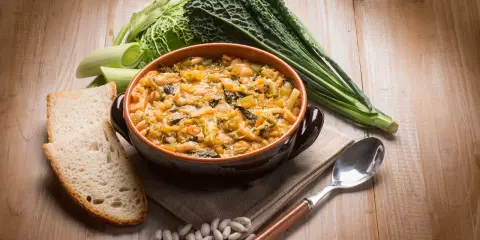 Piatto tipico toscano con pane raffermo: ribollita fumante in ciotola, contornata da fagioli, cavolo nero e porri.