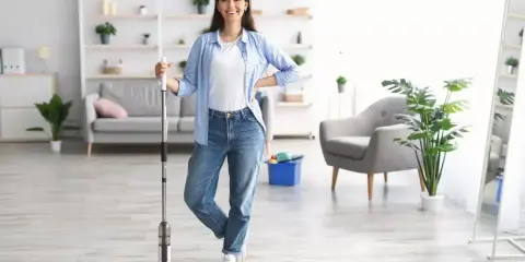 Uśmiechnięta kobieta z mopem w ręku, gotowa do mycia podłogi w jasnym salonie.