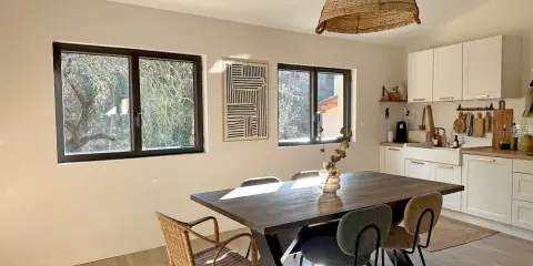 Comedor y cocina luminosos con mesa de madera, sillas de mimbre y tapizadas, y ventanas de cristal térmico que dejan ver el exterior.