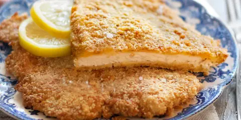 Due cotolette al forno dorate e croccanti, servite su un piatto blu e bianco con spicchi di limone.