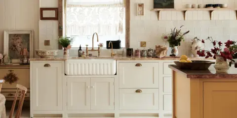 Urocza kuchnia retro inspiracje: białe szafki, ceramiczny zlew, mosiężna armatura, koronkowy zazdrostka i stylowy dywanik.