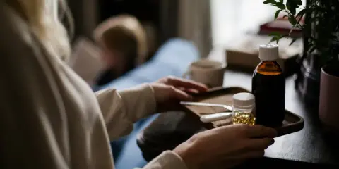 Persona cuida a un niño enfermo, con un termómetro, jarabe y pastillas de paracetamol niños.