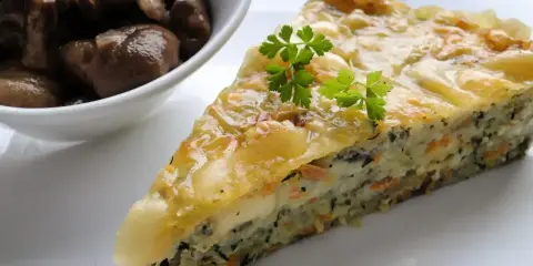 Kawałek zapiekanki z cukinii z warzywami i serem, podany z miseczką pieczarek.