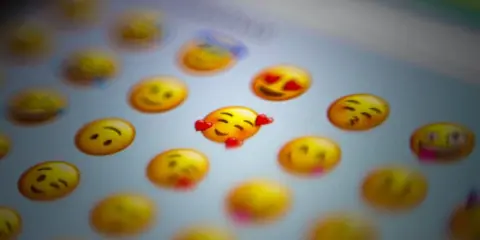 En närbild på en skärm med många gula emoji-ansikten. Ett emoji-ansikte med hjärtögon och ett annat med kyssmun syns tydligt.