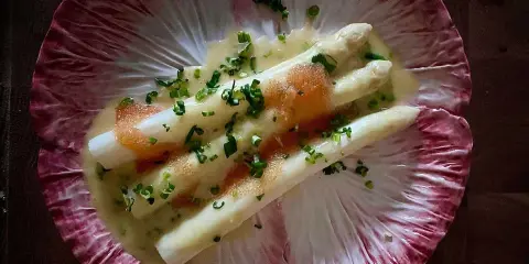 Vitt sparris med en krämig sås, toppad med kaviar och gräslök, serverad på ett rött endiveblad. En delikat ansa sparris.
