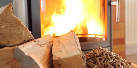 Bûches et granulés de bois prêts pour le chauffage au bois, avec un poêle crépitant en arrière-plan.