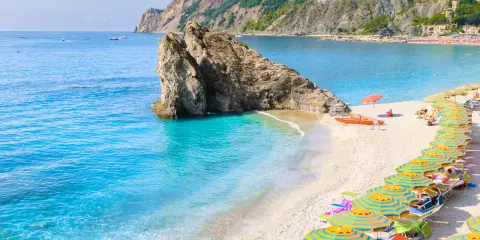 Ein malerischer italien strand mit türkisfarbenem Wasser, einem Felsen im Meer und vielen bunten Sonnenschirmen.