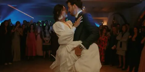 Novios bailando su vals boda, rodeados de invitados expectantes. La novia, con un vestido blanco voluminoso, es alzada por el novio.
