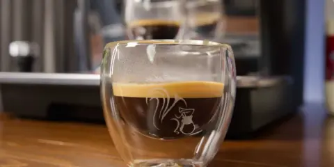 Ein dampfender doppio macchiato in einem doppelwandigen Glas mit einem Eichhörnchen-Motiv.